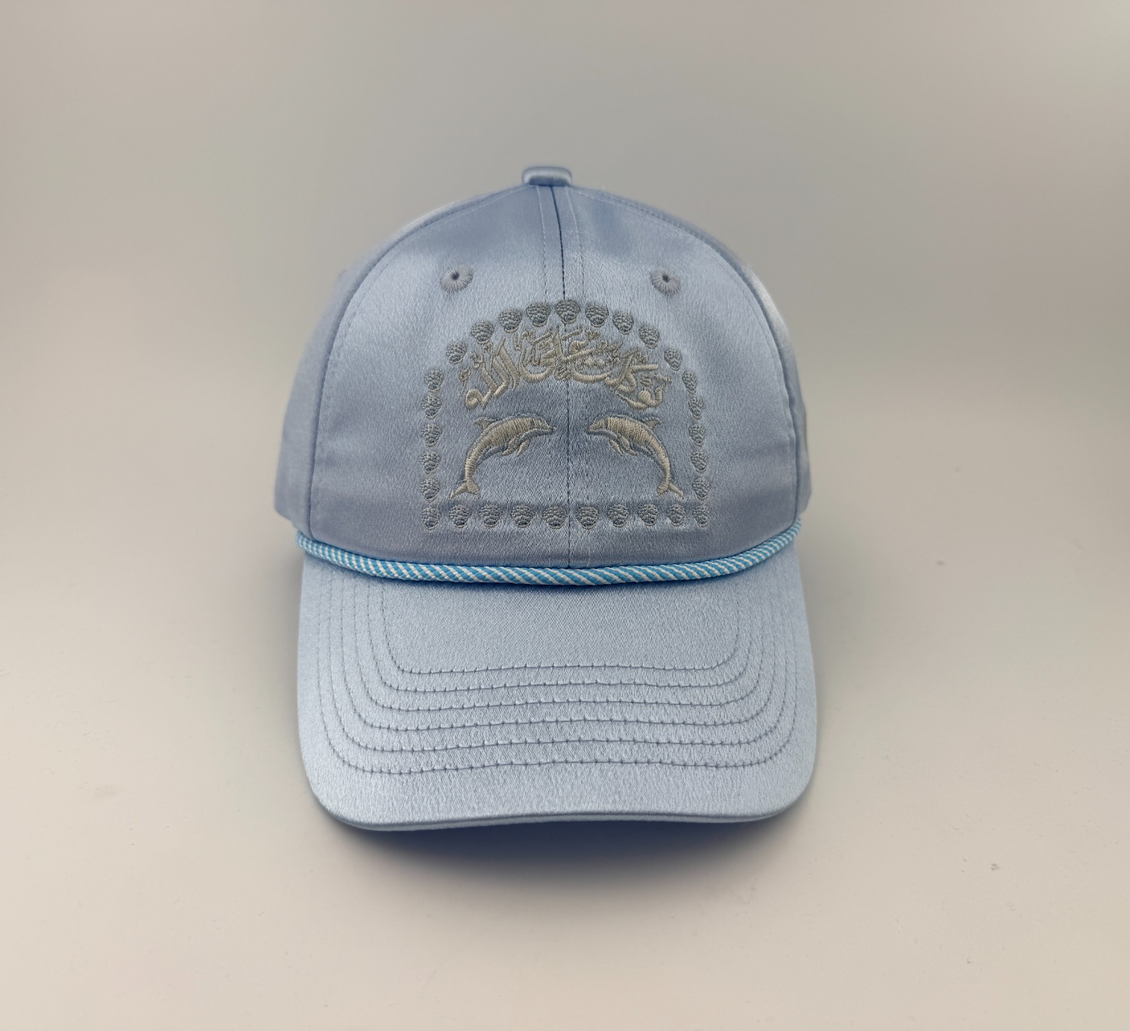 Casquette bleu ciel satinée brodée de deux dauphins, de coquillages et de calligraphie arabe, vue de face