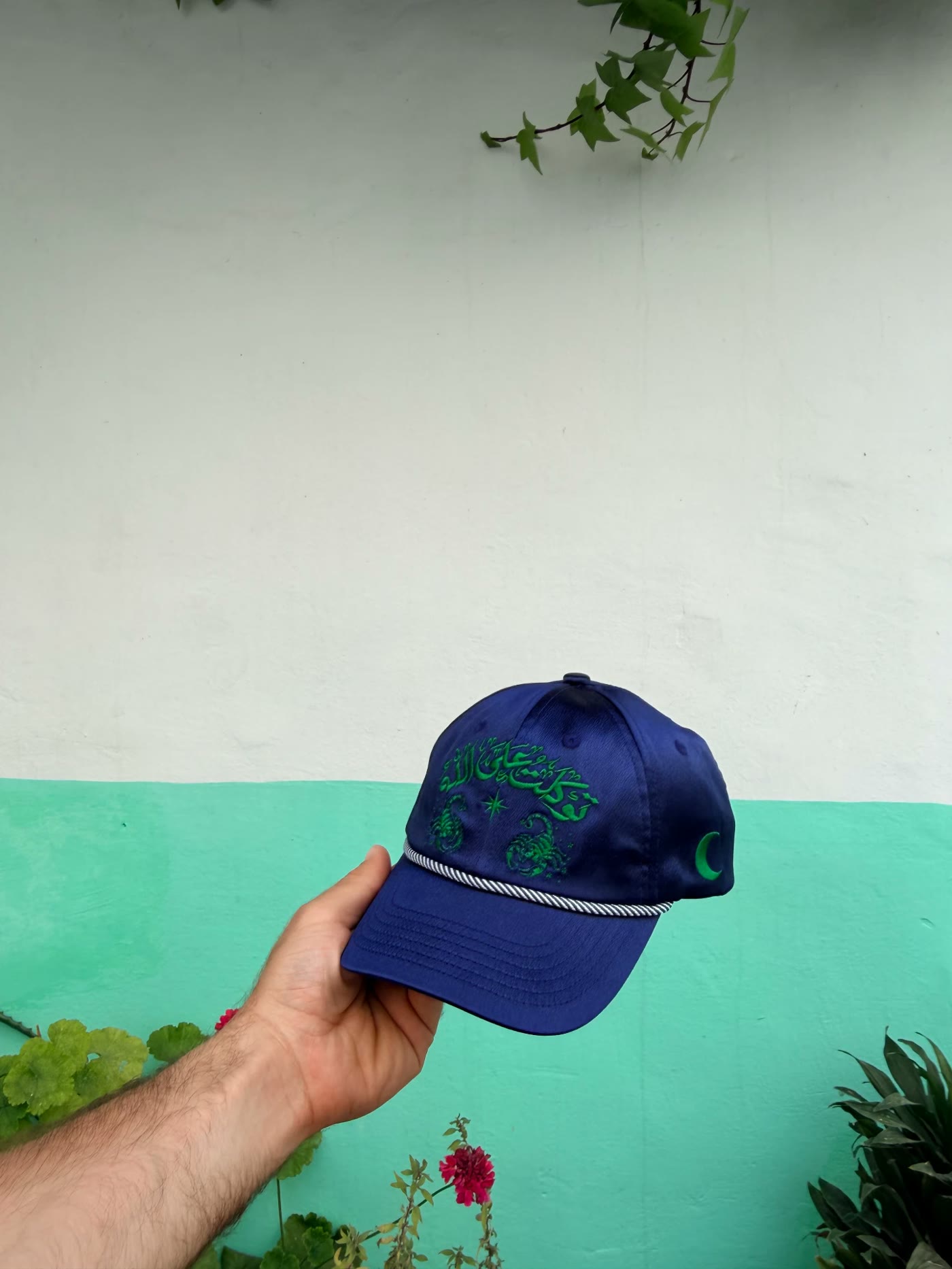 Casquette scorpions tenue devant un mur vert d'eau